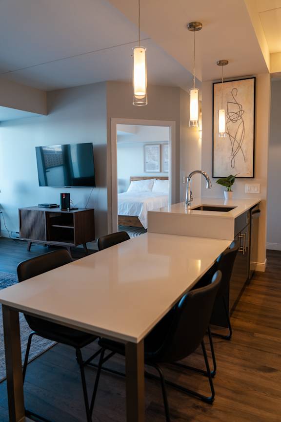 A modern kitchen with a long white table and black chairs.