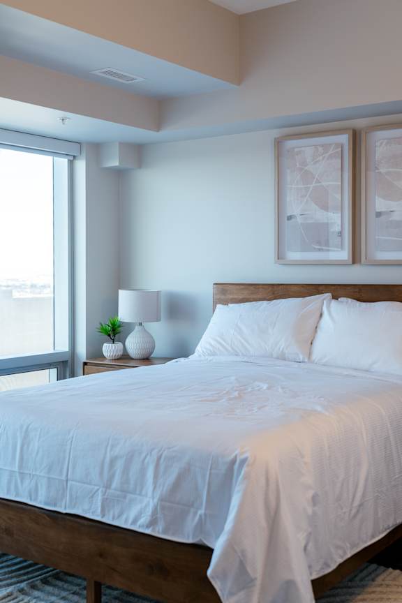 A bed with white bedding sits in a room with a window.