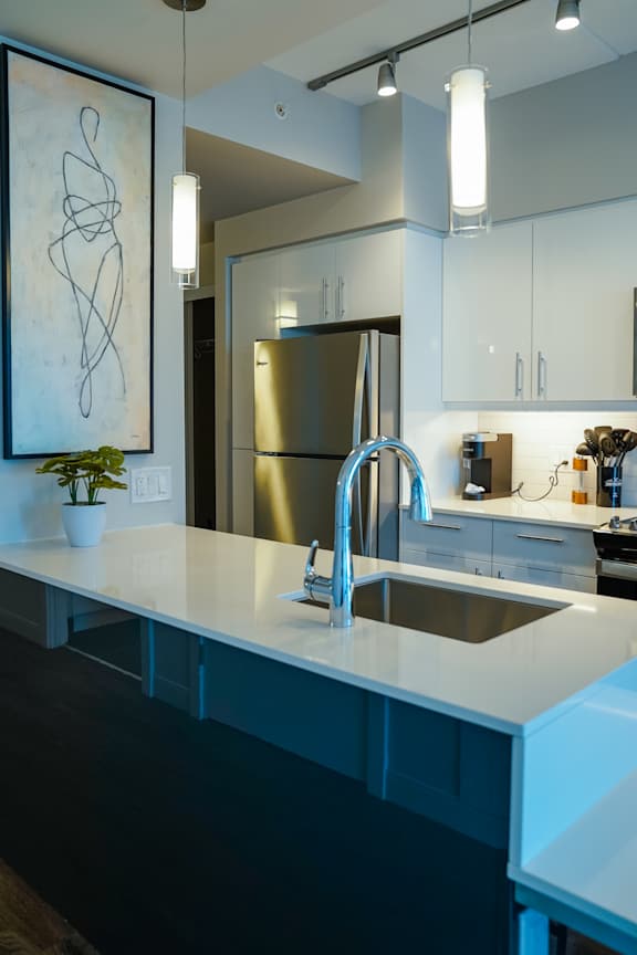 A modern kitchen with a large island and a stainless steel refrigerator.
