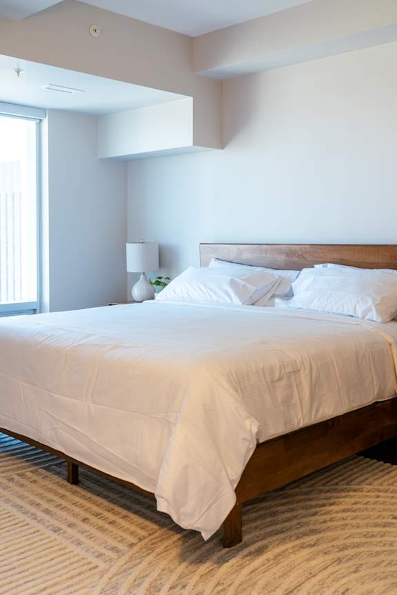 A bed with white sheets and a white lamp on a side table.