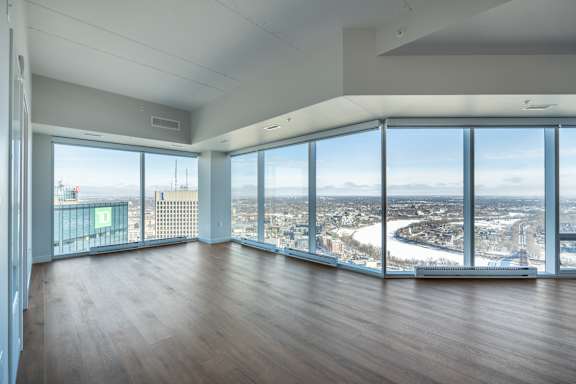 A large empty room with wooden floors and a view of the city through the windows.