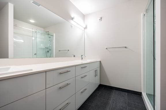 A white bathroom with a sink, mirror, and shower.