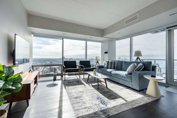 A living room with a grey couch and a large window overlooking the city.