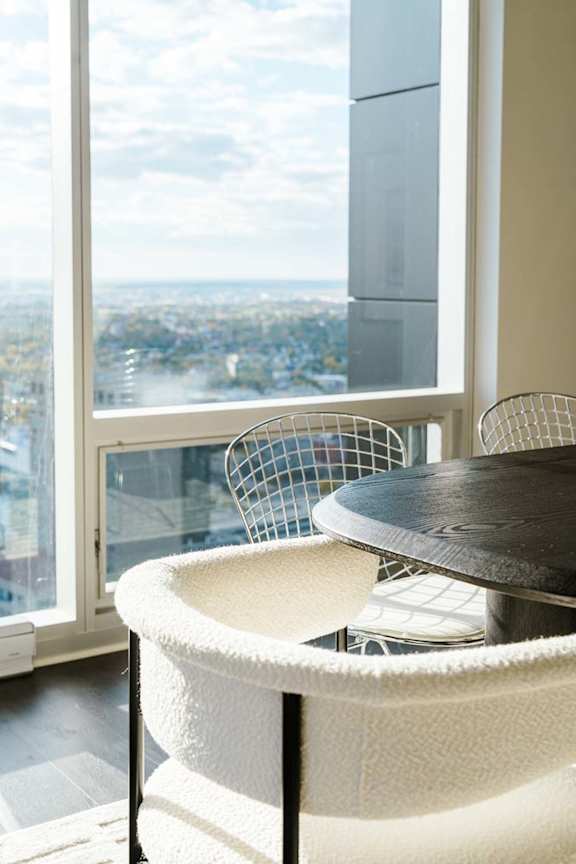 A round table with a black top and a white woven chair in front of a window with a view of a cityscape.