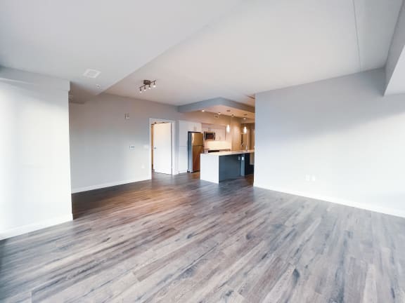an empty living room with hardwood floors and a kitchen in the background