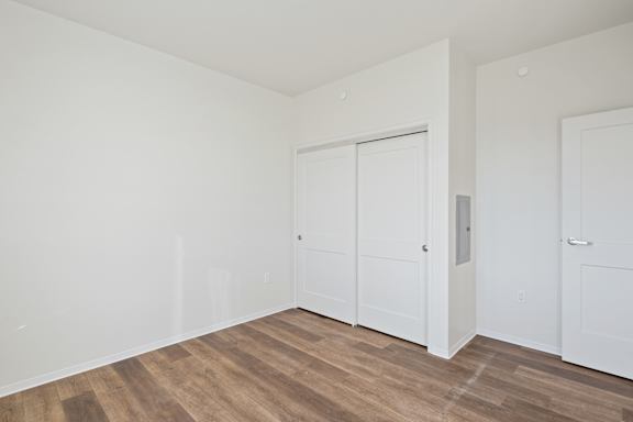 A room with white walls and wood flooring with three white doors.