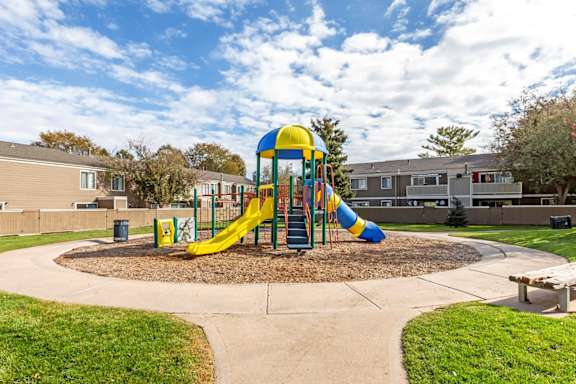 A playground with a yellow and blue slide in the middle of a grassy area.