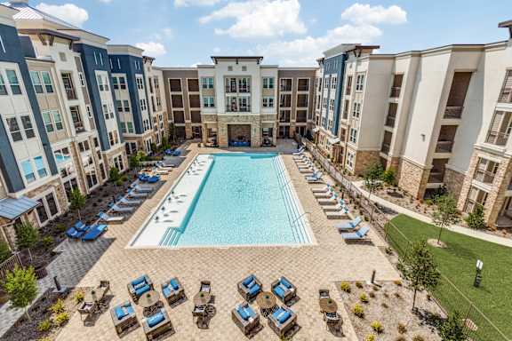 A large swimming pool surrounded by lounge chairs and umbrellas in a courtyard surrounded by apartment buildings.