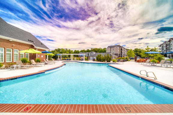 a swimming pool with lounge chairs and umbrellas in front of a brick building at Meridian Obici, Suffolk, VA 23434