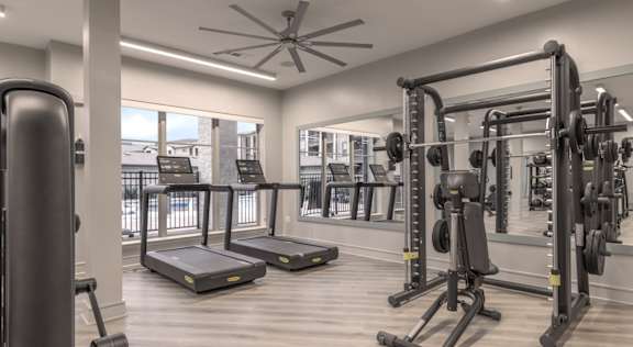 A spacious gym with treadmills, weights, and a ceiling fan.at The Bridge at McKinney, Texas, 75069