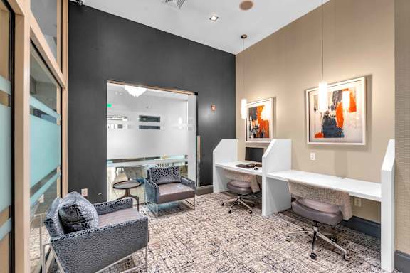 A modern office space with a glass wall, grey chairs, and a white desk.