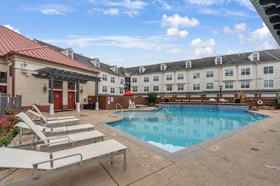 A pool area with sun loungers and a building in the background.