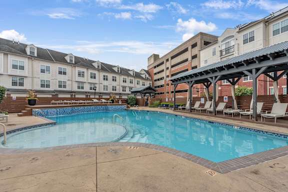 A large swimming pool in front of a building with lounge chairs around it.