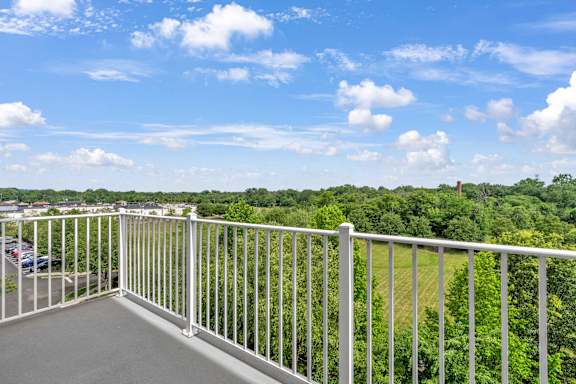 A balcony with a white railing overlooks a green landscape.