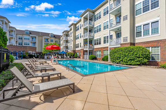 A pool area with sun loungers and a red umbrella in front of apartment buildings.