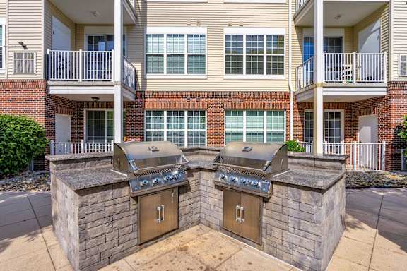 Two outdoor BBQs are built into the side of a brick building.