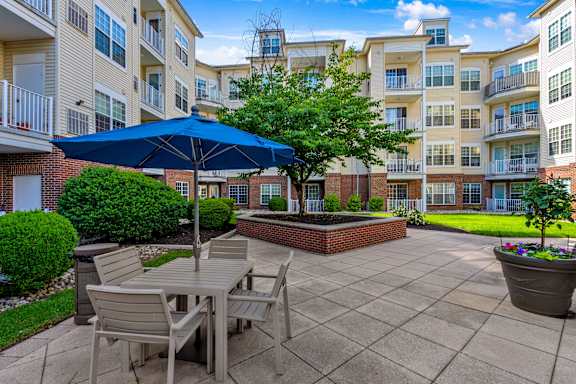 A patio with a table and chairs under an umbrella with apartment buildings in the background.