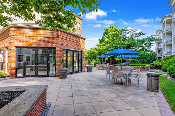 A patio with a table and chairs is surrounded by a brick building and trees.