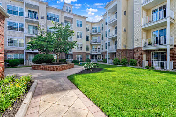 A sunny day at a brick apartment complex with a walkway and green grass.