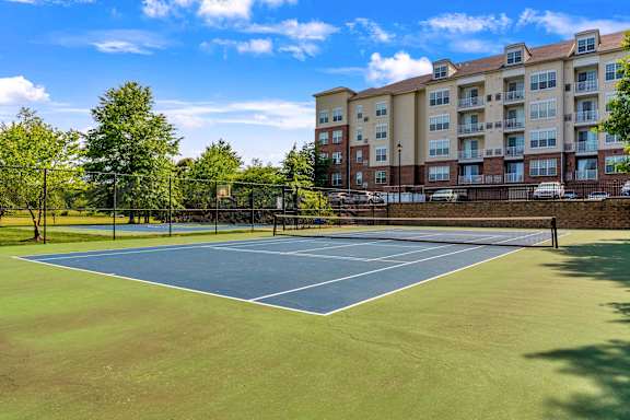 A tennis court is surrounded by a fence and apartment buildings.