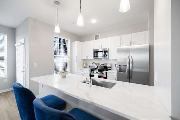 A modern kitchen with a white countertop and blue chairs.