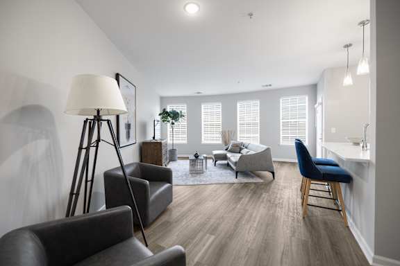 A well-lit living room with a grey sofa, a black chair, and a wooden floor.