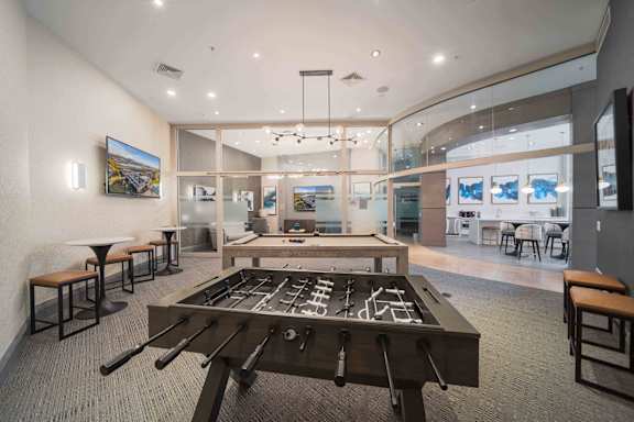 A room with a foosball table in the center and a bar area to the left at Harbor Pointe Apartments, Bayonne 07002