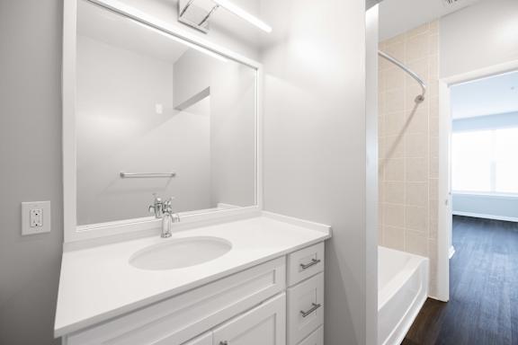 A white bathroom with a sink, mirror, and bathtub.