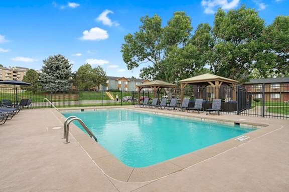 A swimming pool surrounded by a black fence and trees at Mountain Vista Apartments, Lakewood, CO, 80228