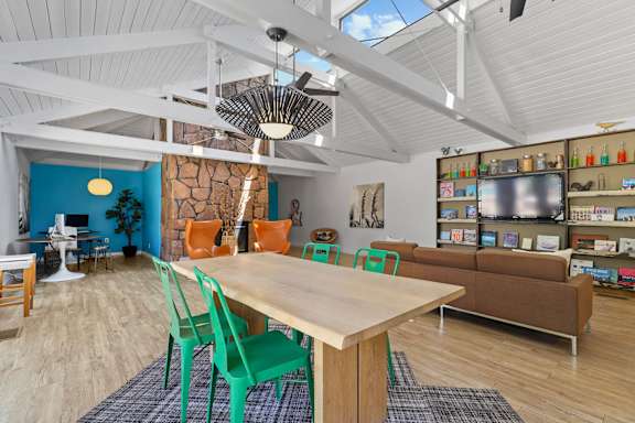 A room with a table and chairs in the foreground and a shelving unit in the background.