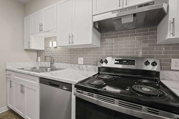 A kitchen with a stove, sink, and cabinets.