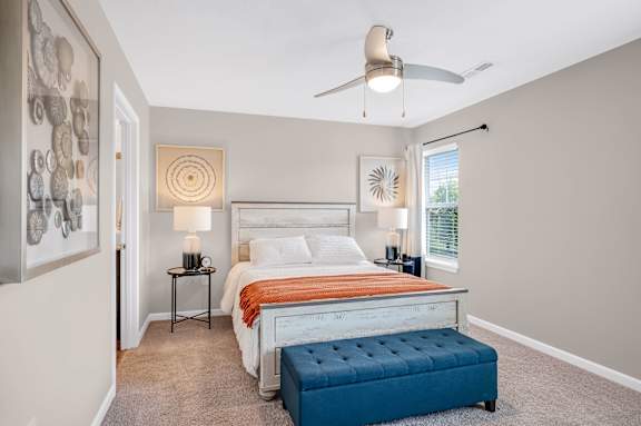 A bedroom with a bed, a bench, and a ceiling fan.