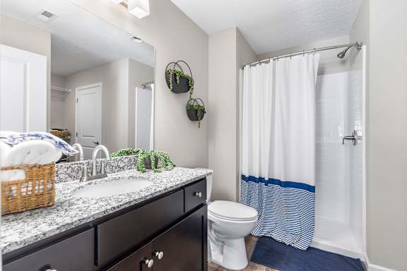 A bathroom with a white toilet, a sink with a marble countertop, and a shower with a white curtain.