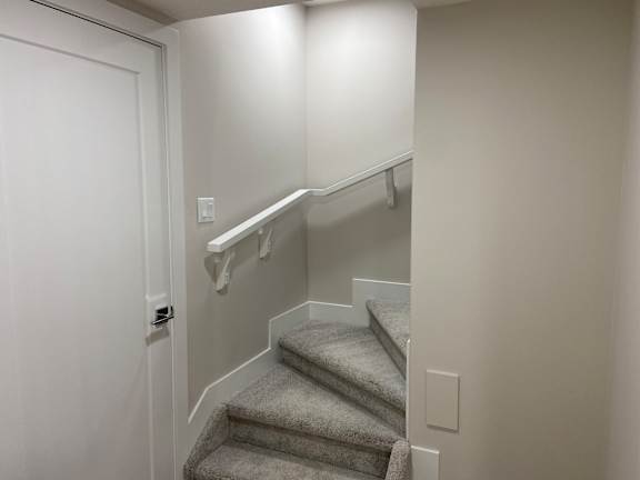 A stairway with a grey carpeted runner and white handrails.