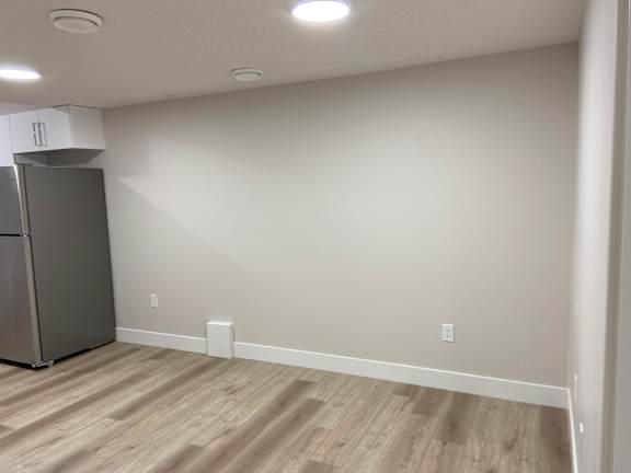 A kitchen area with a refrigerator and wooden flooring.