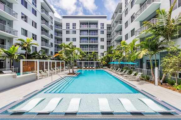 A large swimming pool surrounded by lounge chairs and palm trees. at Morea Apartments, Pompano Beach, 33062