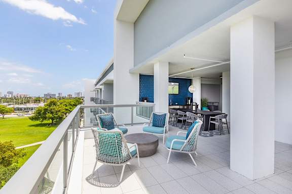 A balcony with a table and chairs overlooking a green field. at Morea Apartments, Pompano Beach, 33062