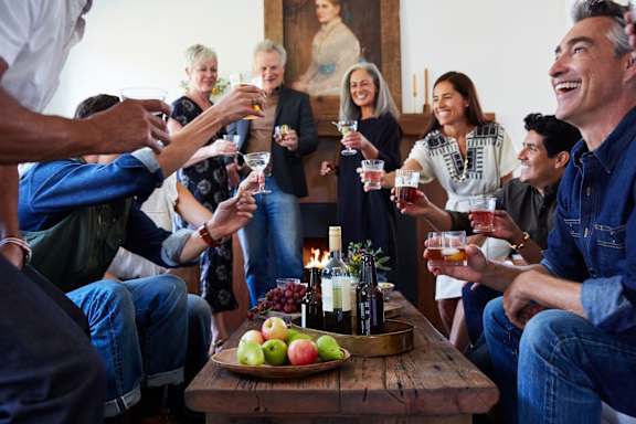 A group of people are gathered around a table, toasting with drinks and enjoying a meal.