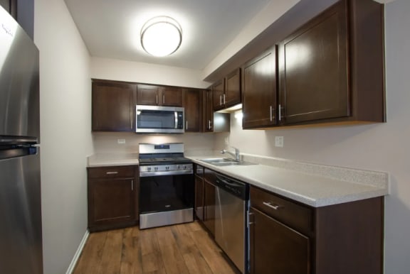 Kitchen with Dark Wood Cabinetry and  Granite Countertops at The Greenway at Carol Stream Apartments