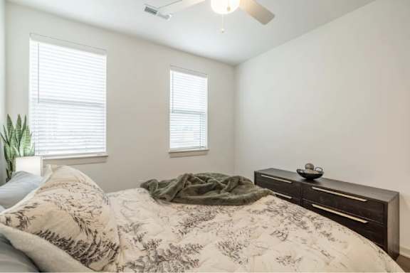 A bedroom with a bed, a plant, and a ceiling fan.
