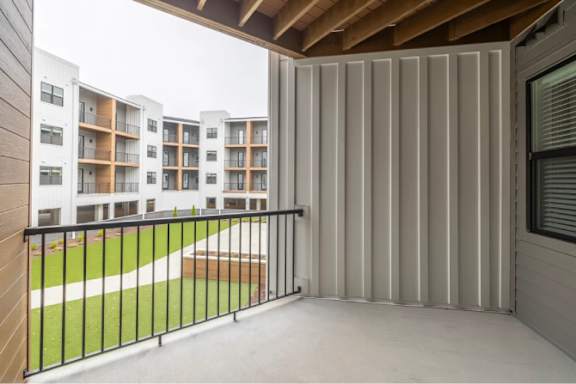 A balcony with a black railing overlooks a grassy area and apartment buildings.