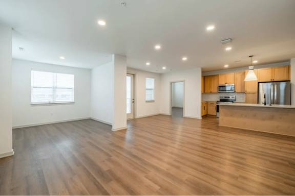 A spacious room with wooden floors and a kitchen area in the background.