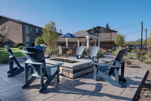 A patio with chairs and a table in the foreground with a building in the background at The Greenway at Carol Stream, Carol Stream