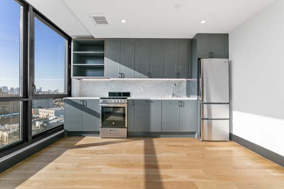 Modern kitchen with gray cabinetry and city views at 1134 Fulton Street Apartments, New York, 11216