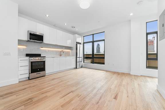 A spacious living room with wooden flooring and a large window overlooking a city skyline.