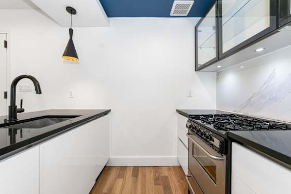 A modern kitchen with black countertops and a wooden floor.