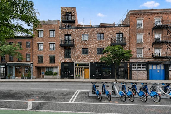 A row of bikes are parked on the sidewalk in front of a brick building.
