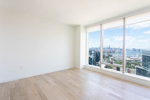 Empty room with wooden floor and large windows overlooking a cityscape.