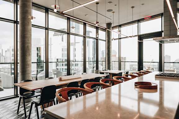 a long communal table and chairs in a restaurant with large windows at The Lively, Jersey City, 07302