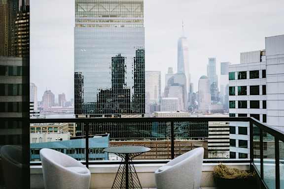 a view of the city skyline from a balcony with chairs and a table at The Lively, Jersey City, NJ